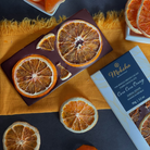 Moksha Chocolate 70% Single Origin Cacao Dark Chocolate from Zorzal Estate, Dominican Republic, topped with dried Cara Cara orange slices, displayed on a dark background with a vibrant orange cloth.